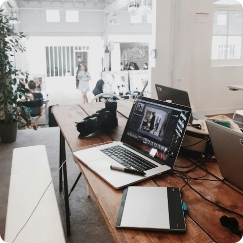 a camera, tablet, and three laptops sitting on a table with people standing in the background